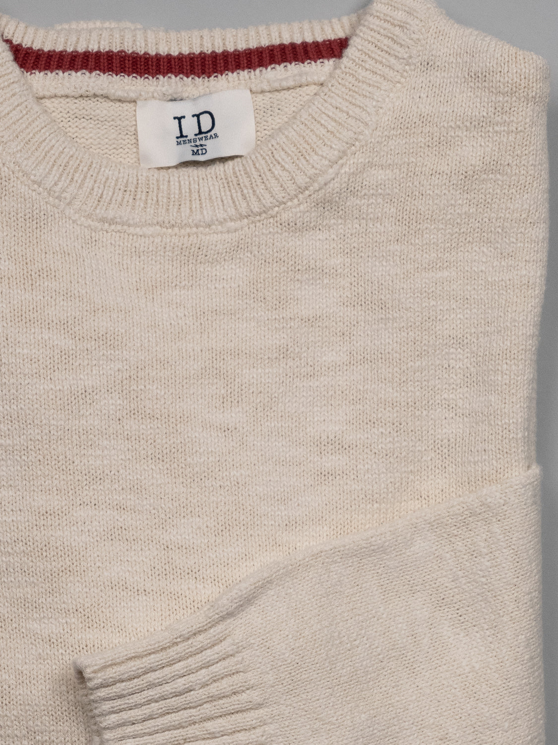 The Odense Slub Yarn Sweater by ID Menswear is a beige, regular fit knit crew neck with an ID label and Medium size at the neck. It elegantly rests on a light gray surface, showcasing its round neckline design.