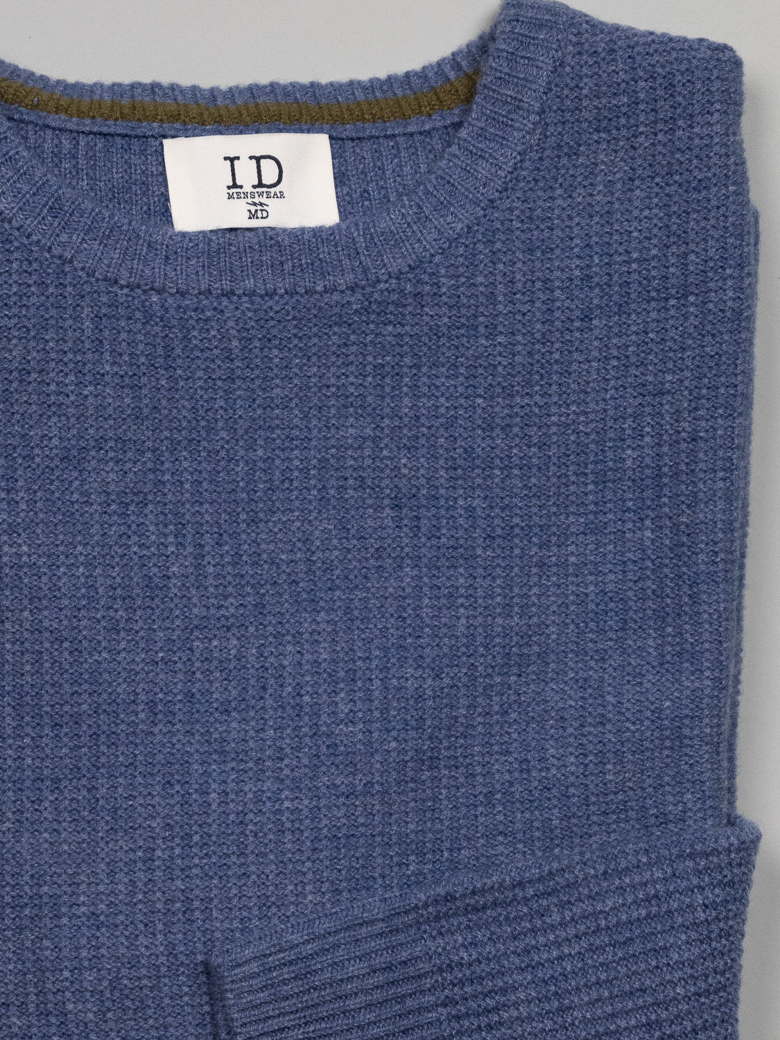 The Uppsala Merino Wool Sweater by ID Menswear features a blue textured knit with a round neckline and ribbed popcorn stitch, ideal for chilly weather. Inside, a visible ID Menswear label complements the waffle-like pattern of the fabric.