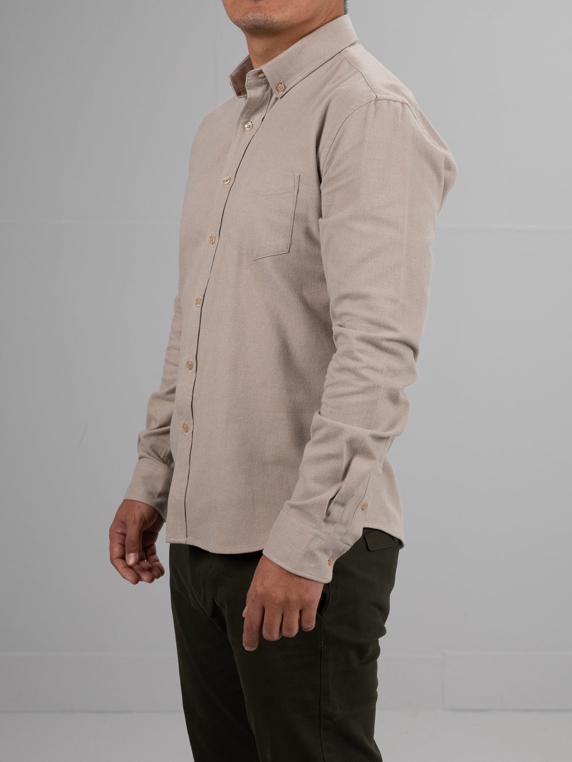 A man stands sideways wearing the Rex Cotton Sustans Blends Flannel Shirt by ID Menswear in light beige with long sleeves, paired with dark pants, against a plain gray background. His face is partially out of frame.