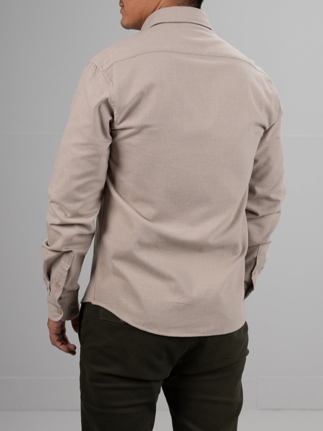 A person stands with their back to the camera, wearing the ID Menswear Rex Cotton Sustans Blends Flannel Shirt in light beige and dark green pants, set against a plain gray background.