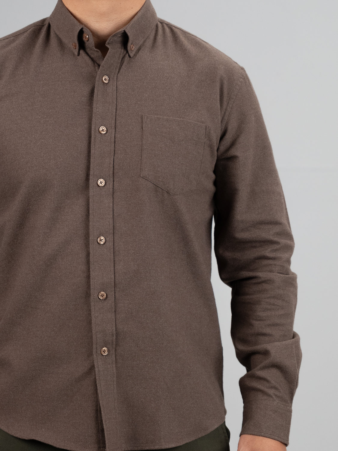 A person wears the ID Menswear Rex Cotton Sustans Blends Flannel Shirt, a brown, long-sleeve, button-up with a front pocket, shown from shoulders to waist against a plain light gray background.
