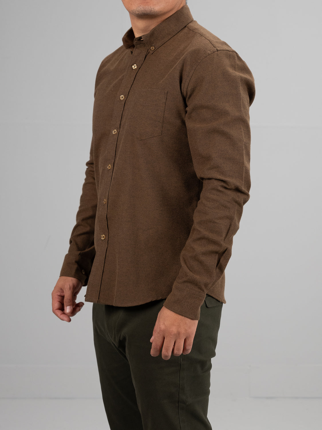 A person in a Magnus Brushed Twill Solid Flannel Shirt by ID Menswear, featuring a button-down collar, chest pocket, and long sleeves, pairs it with dark green pants against a plain gray background. Their face is not visible.