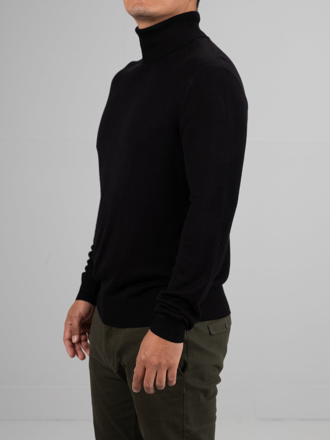 A person in an Oregon Viscose Turtle Neck by ID Menswear, known for its soft texture, and olive green pants stands against a plain gray background. Their face remains unseen.