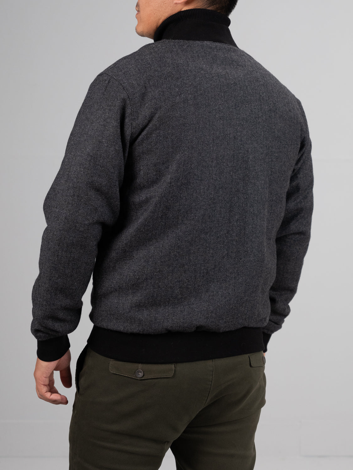 A person dressed in an olive green Montauk Wool Blend Jacket by ID Menswear with matching pants stands facing away, head slightly turned. The neutral background highlights the lightweight comfort of their outfit.