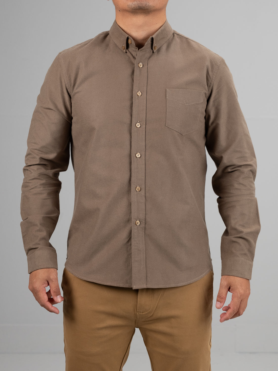 A person in a Milo Brushed Oxford Flannel Cotton Shirt by ID Menswear, paired with beige pants, stands against a gray background. The brown shirt features a chest pocket and long sleeves, matching the relaxed pose with hands at their sides.