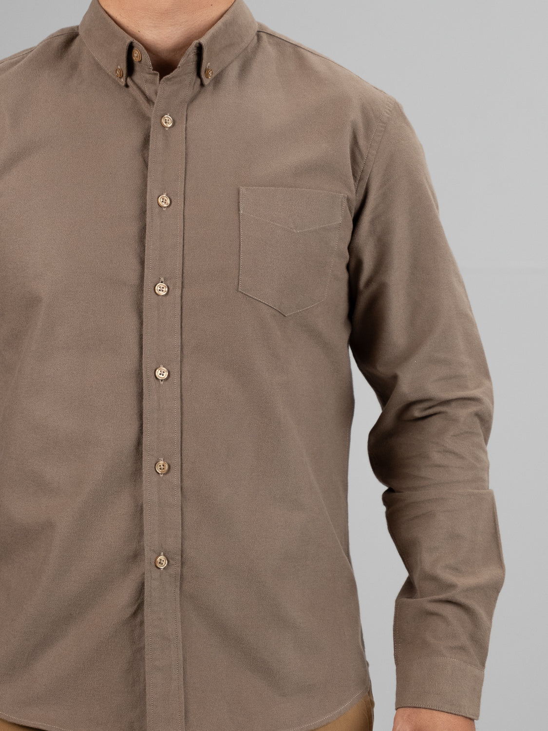 A person wearing the ID Menswear Milo Brushed Oxford Flannel Cotton Shirt, featuring a chest pocket and rolled-down sleeves, stands sharply in a khaki button-up design against a plain gray backdrop.