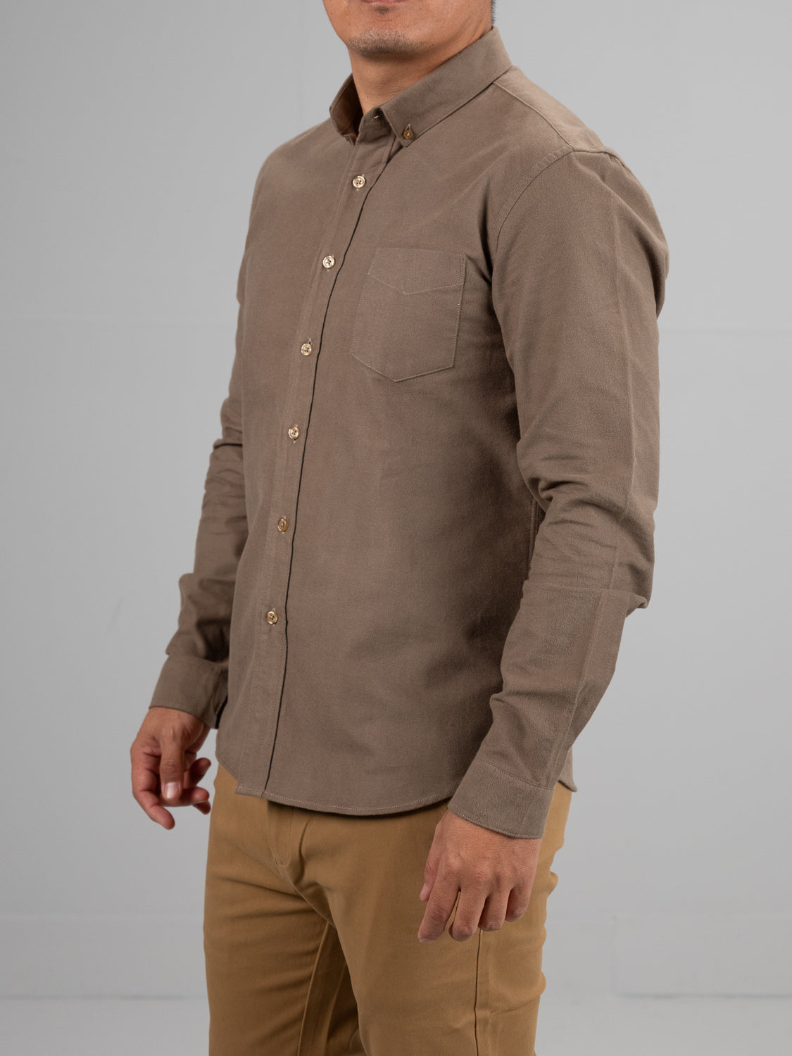 A person in an ID Menswear Milo Brushed Oxford Flannel Cotton Shirt in beige, with a chest pocket, paired with khaki pants, stands against a plain gray background, head partially out of frame.