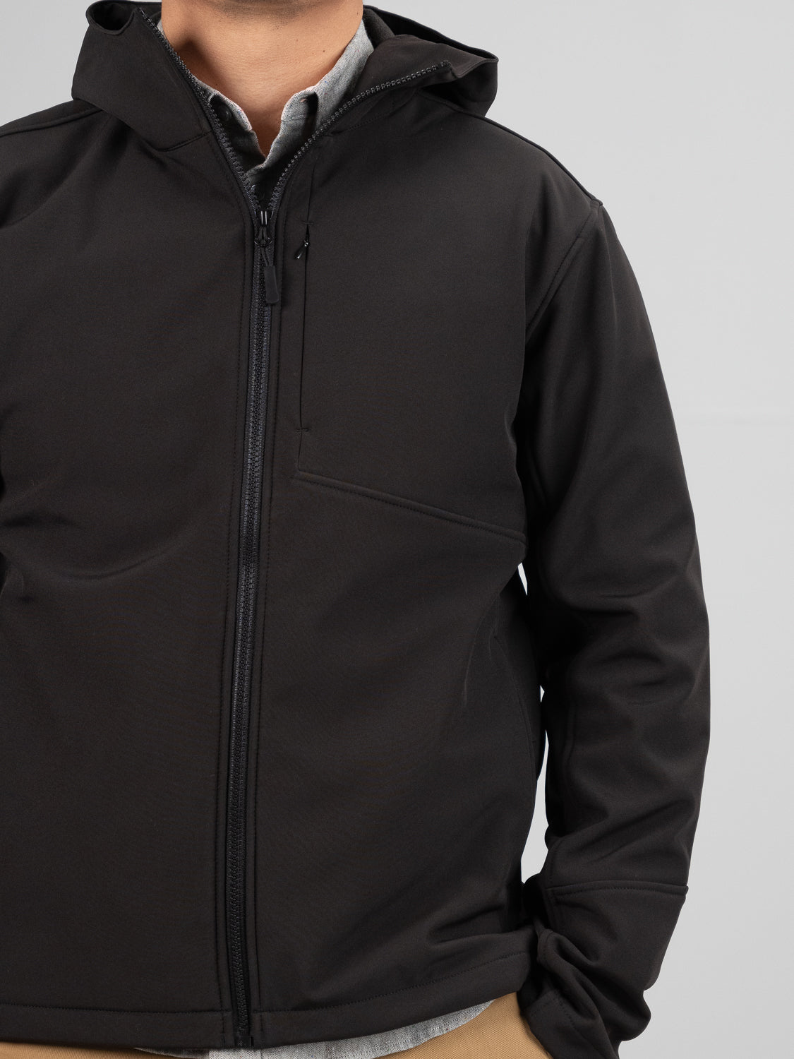 A person wearing the Fairbanks Soft Shell Hooded Jacket by ID Menswear stands against a gray background. The lightweight jacket features a front zipper and chest pocket, and with their hand resting in the pocket, only part of their face is visible, highlighting the regular fit.