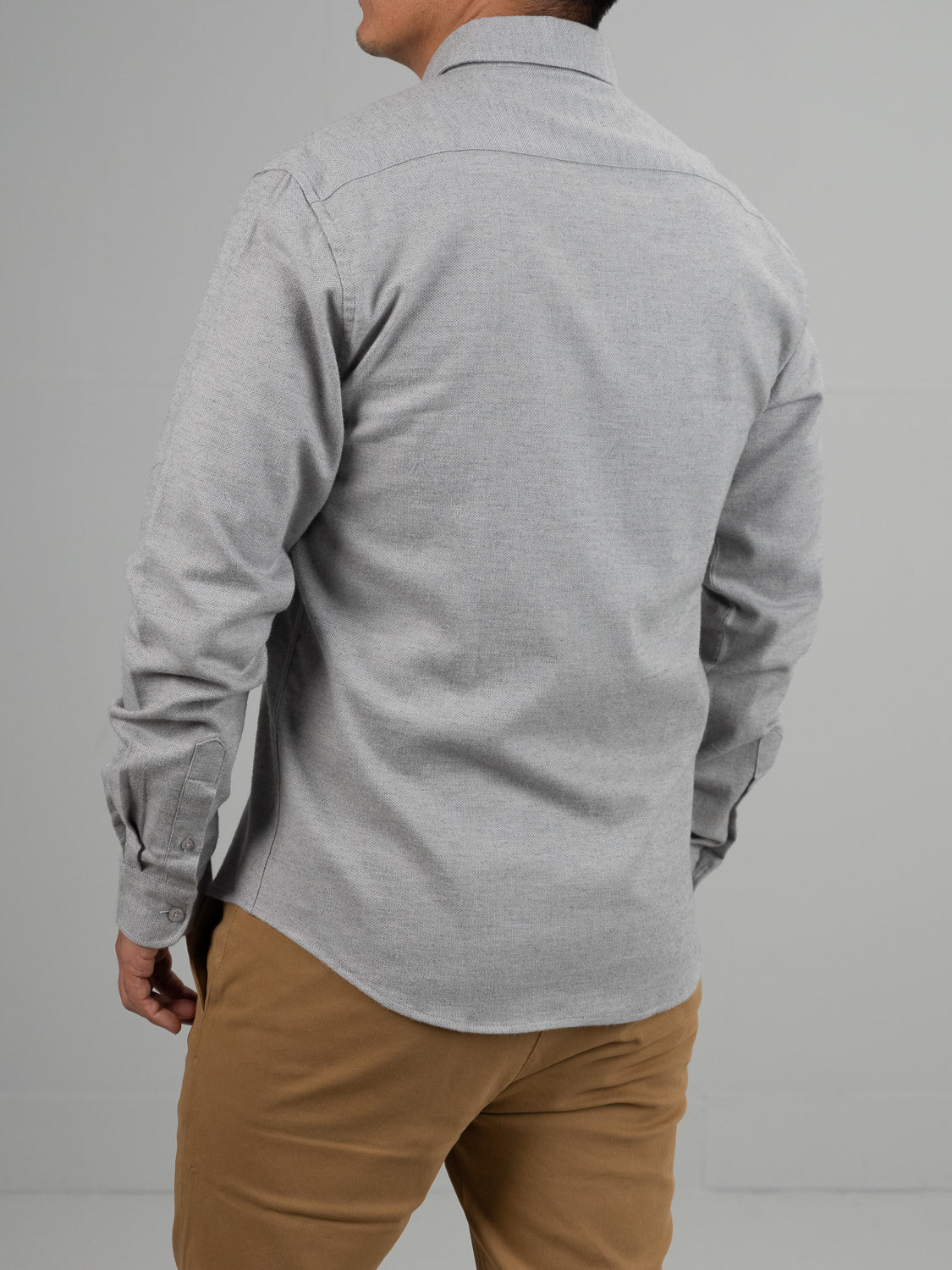 A person in an Amir Solid Flannel Textured Dobby Shirt by ID Menswear, light gray with a dobby weave, pairs it with khaki pants. Facing away from the camera, they emit an aura of lightweight comfort against a neutral backdrop.