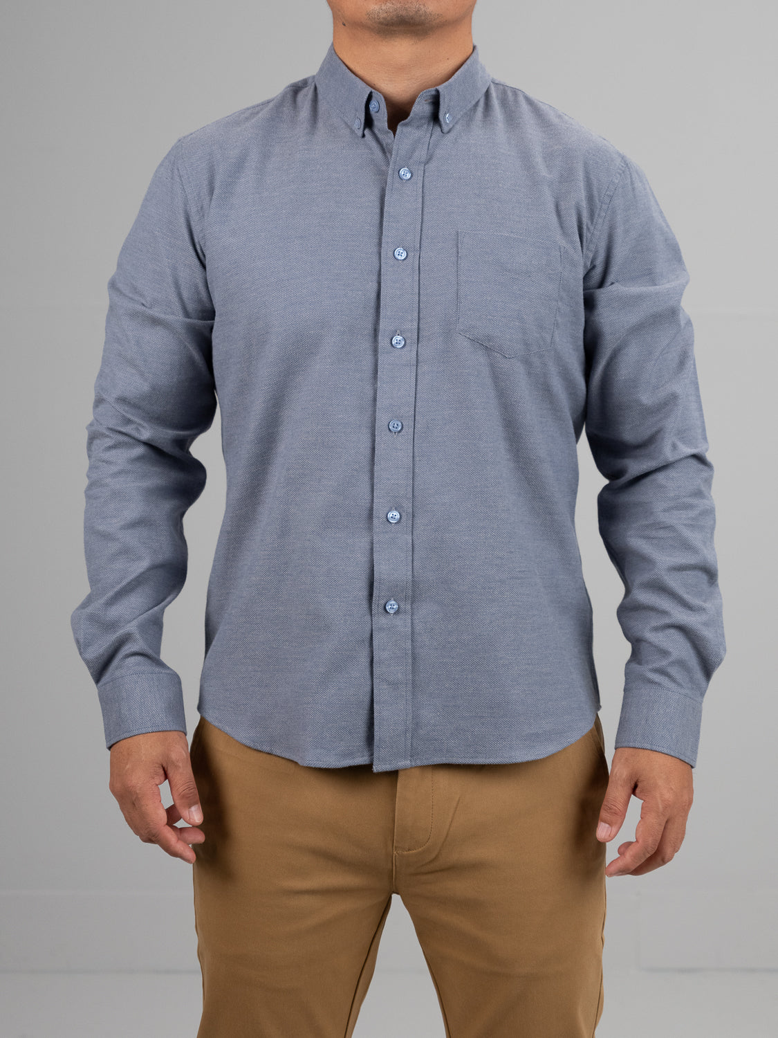A person wears an Amir Solid Flannel Textured Dobby Shirt by ID Menswear, styled with lightweight comfort and a dobby weave. The blue button-up pairs with beige pants against a plain gray background. The left pocket complements the look, although the persons head is not shown.