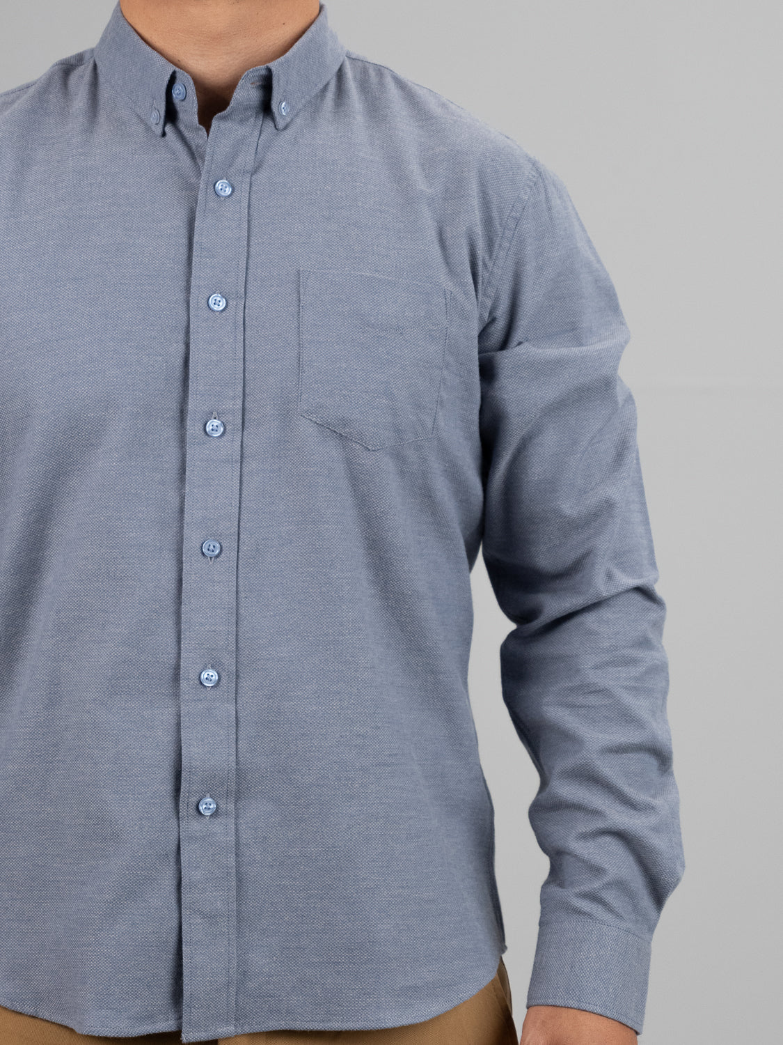 Someone is wearing the Amir Solid Flannel Textured Dobby Shirt in light blue by ID Menswear, featuring a chest pocket, collar, and long sleeves with a lightweight dobby weave. The shot captures their upper body against a plain light gray background with their lower face and head out of frame.