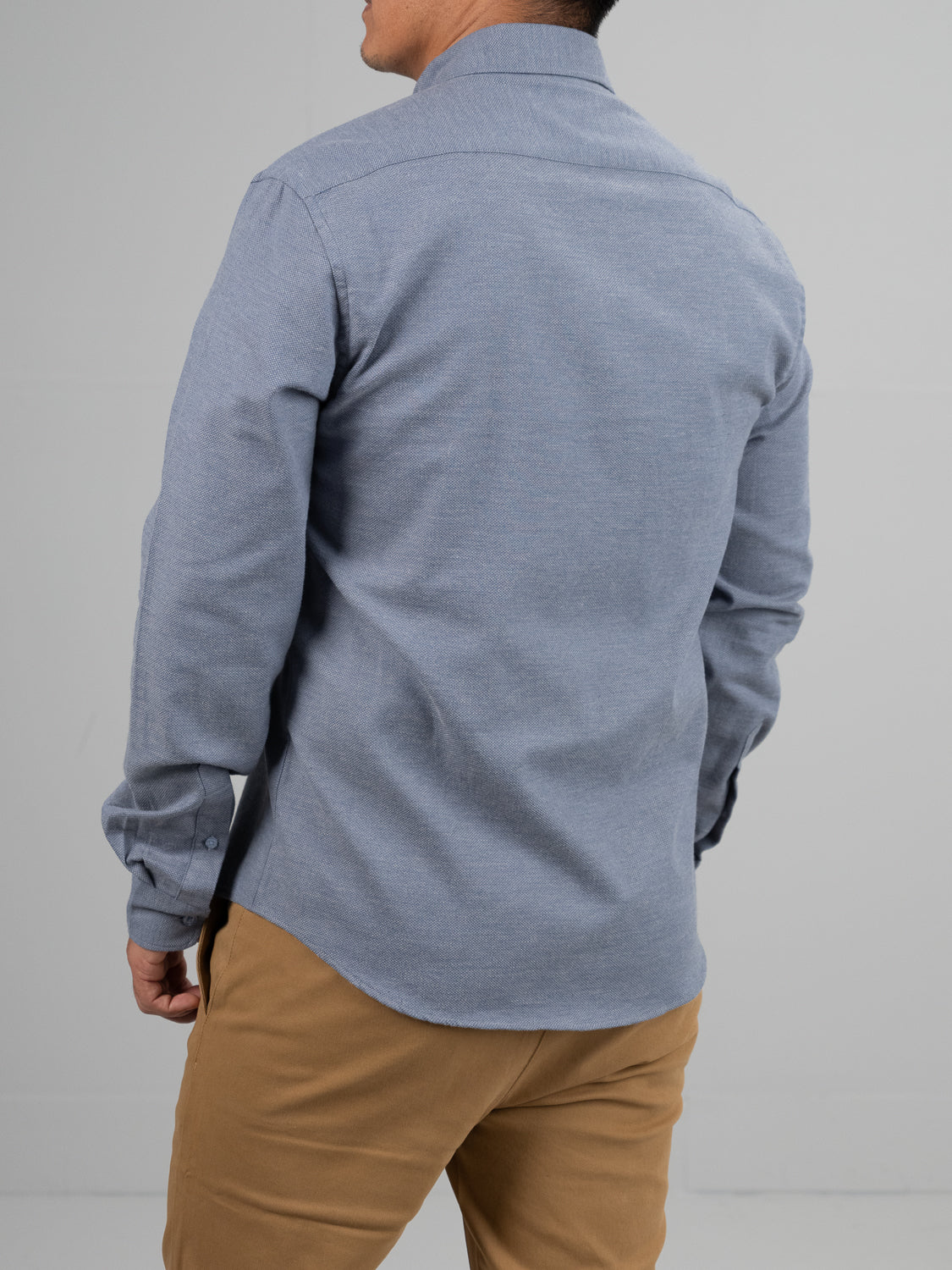 An individual is wearing an Amir Solid Flannel Textured Dobby Shirt by ID Menswear in light blue and khaki pants, standing against a gray background with their back to the camera.
