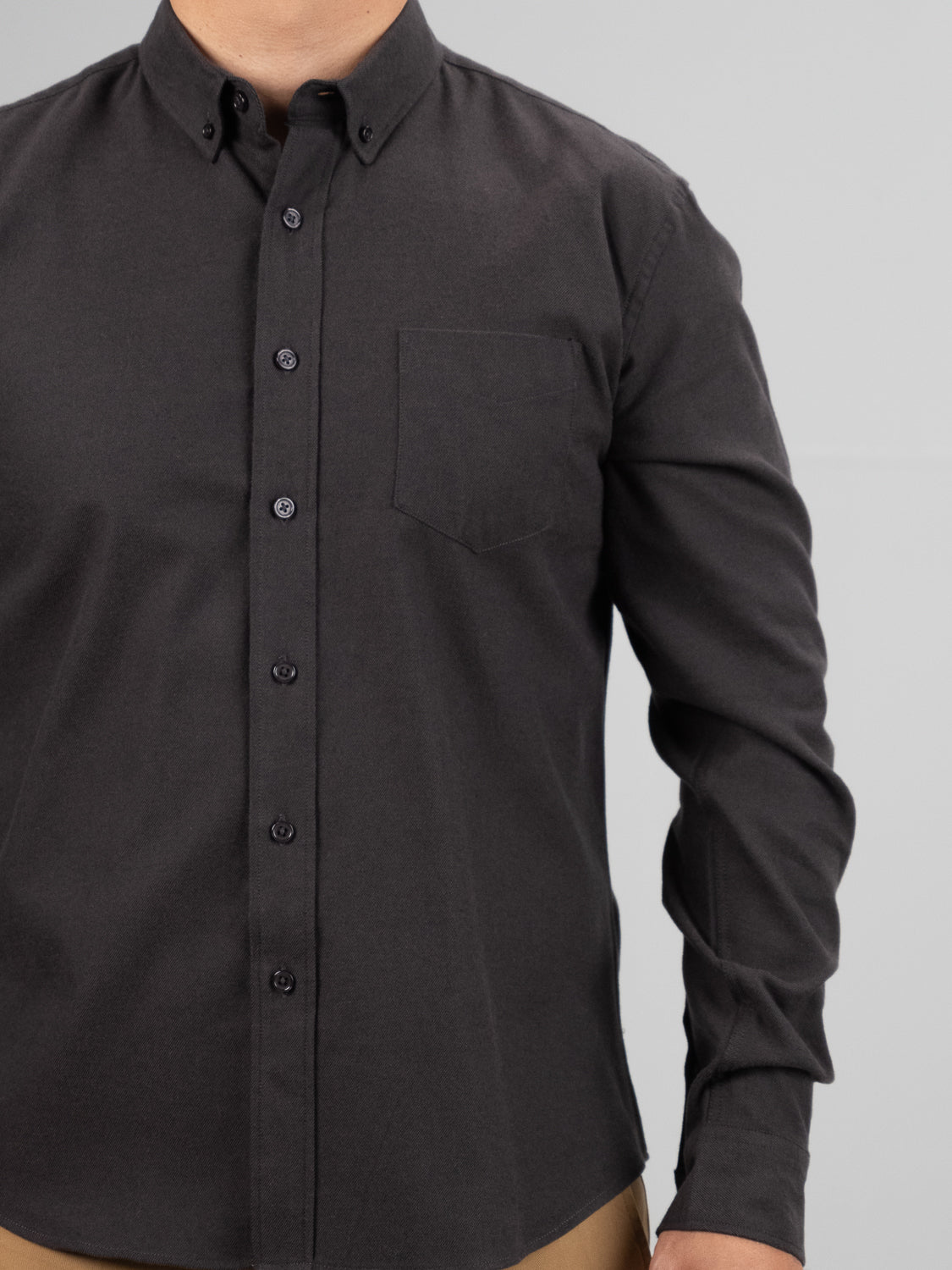 An individual in the Magnus Brushed Twill Solid Flannel Shirt by ID Menswear, featuring a button-down collar and chest pocket, effortlessly pairs it with tan pants against a light gray backdrop.