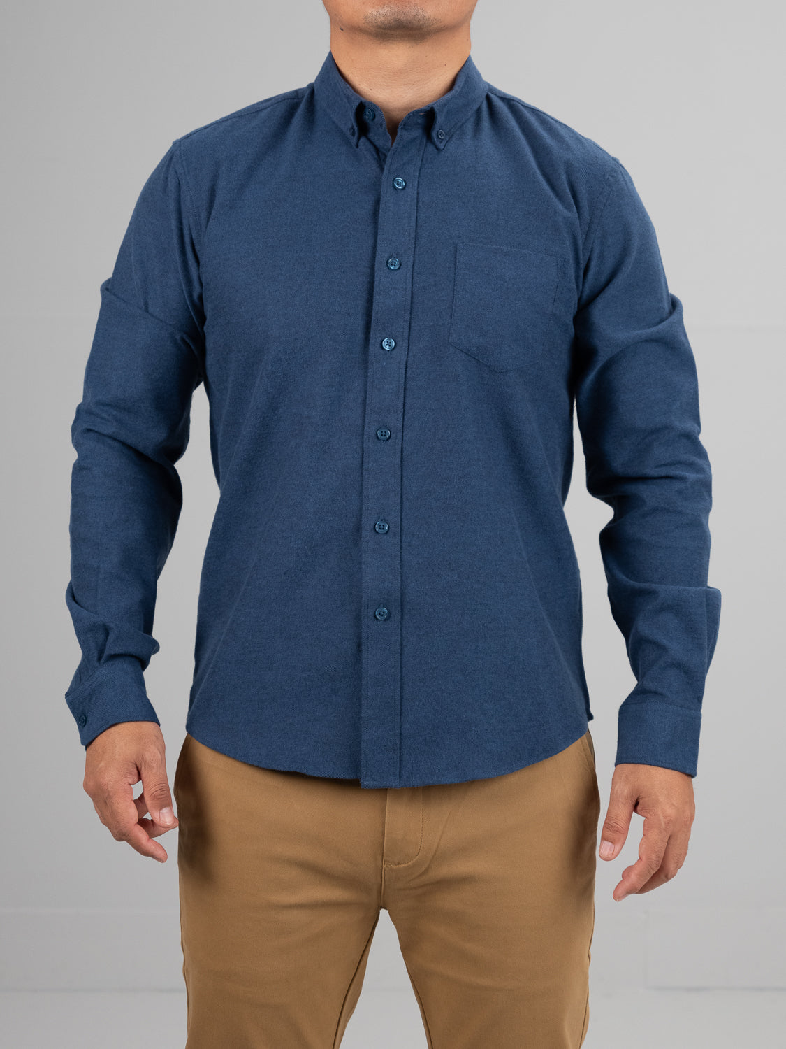 A person wears the ID Menswear Magnus Brushed Twill Solid Flannel Shirt in blue, paired with beige pants, standing against a plain gray background, with their head not visible.