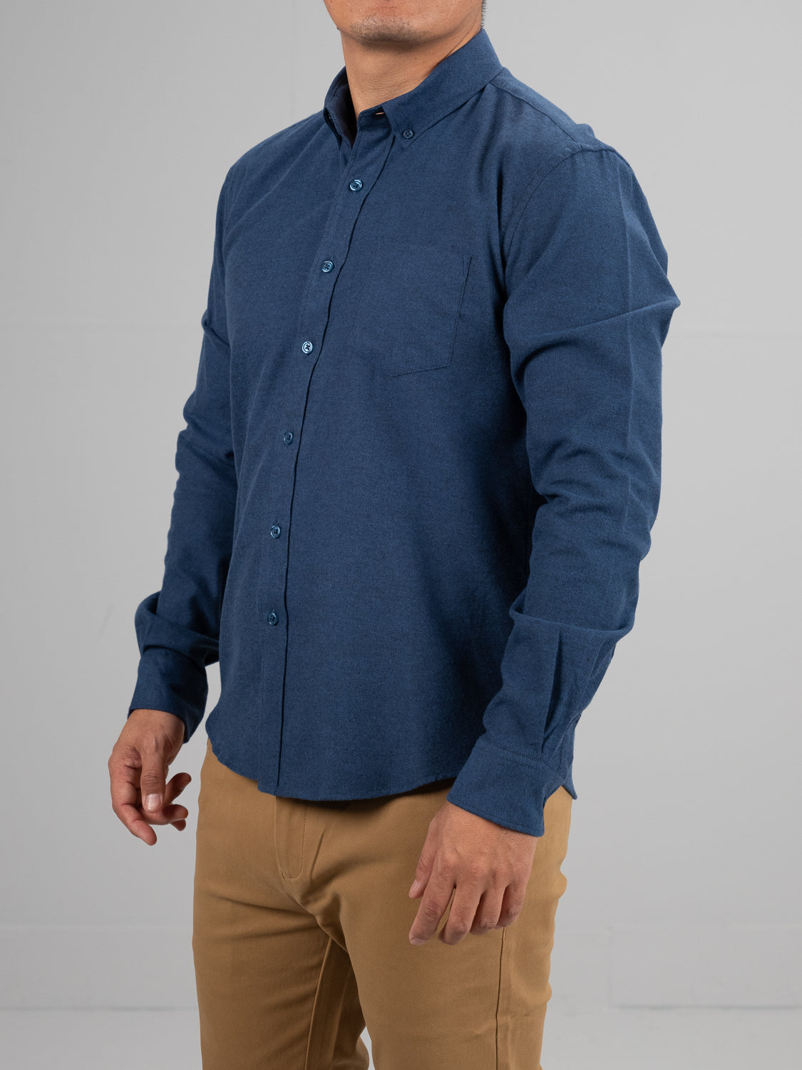 A person in an ID Menswear Magnus Brushed Twill Solid Flannel Shirt, featuring a button-down collar and left chest pocket, pairs it with khaki pants. They stand against a plain gray backdrop, shown neck down with their left arm slightly bent.