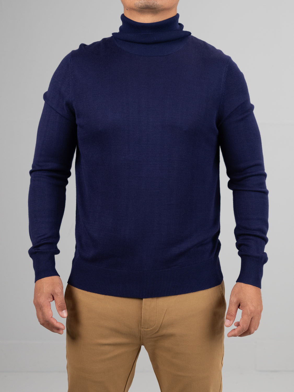 A model wears a navy Oregon Viscose Turtle Neck from ID Menswear with tan pants against a neutral gray backdrop. The soft fabric elegantly drapes as their hands hang naturally, showcasing the everyday appeal of this attire.