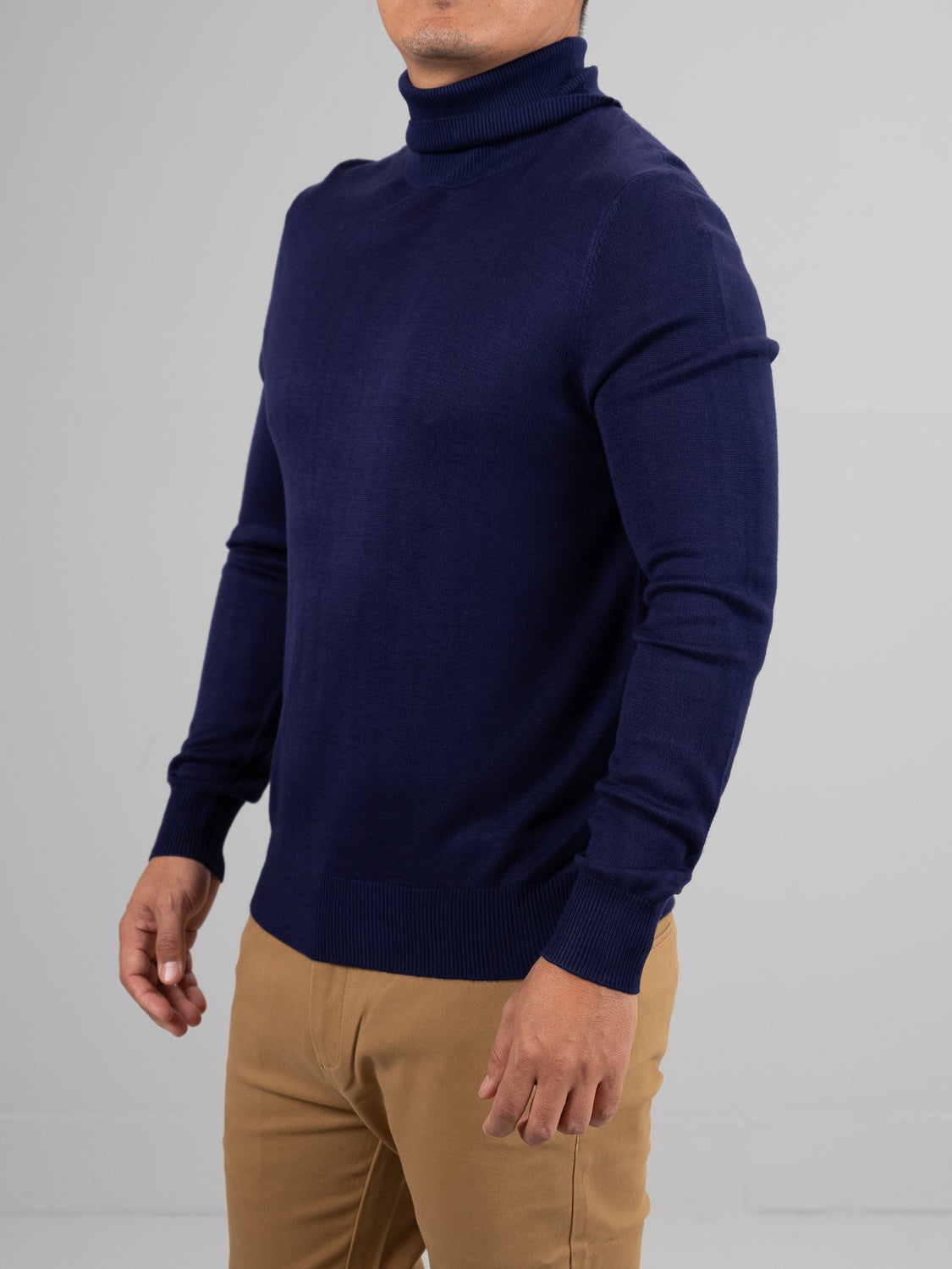 Dressed in an ID Menswear Oregon Viscose Turtle Neck sweater and beige pants, a person poses against a gray backdrop. One arm is forward while the other rests by their side, showcasing both style and comfort. Their face remains unseen.