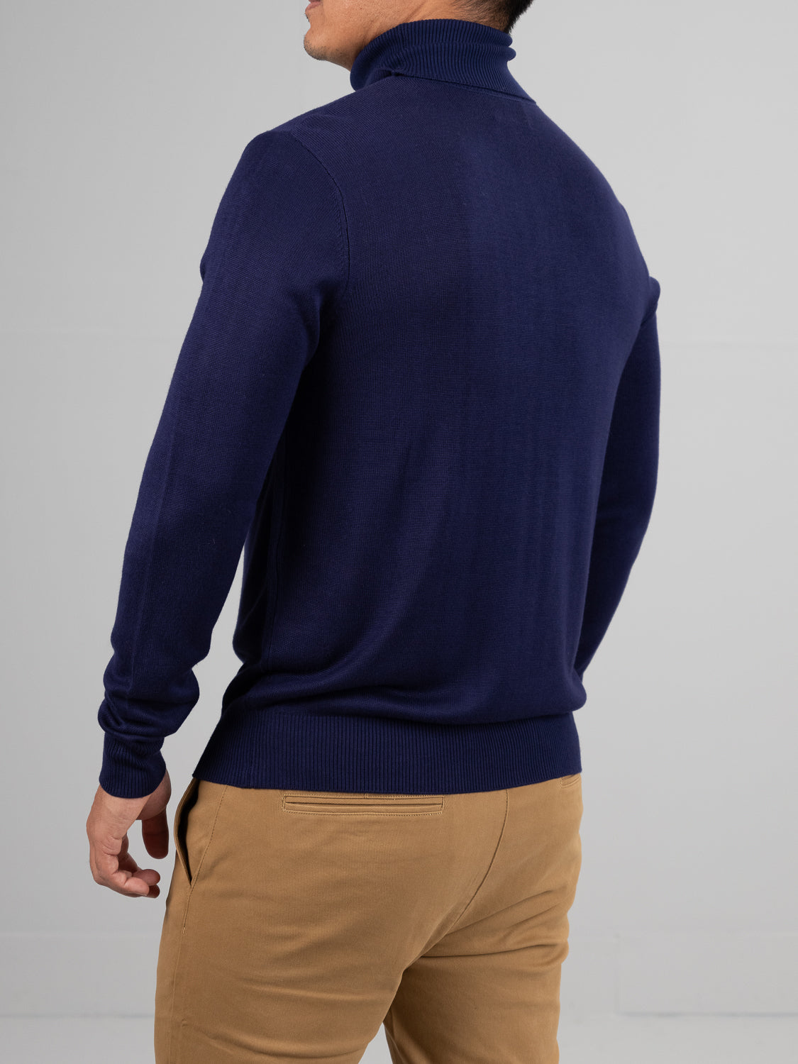 A person in a navy Oregon Viscose Turtle Neck by ID Menswear and beige pants stands back-facing against a plain gray background. The effortlessly chic look, perfect for daily wear, combines style with the sweaters soft touch for added comfort.