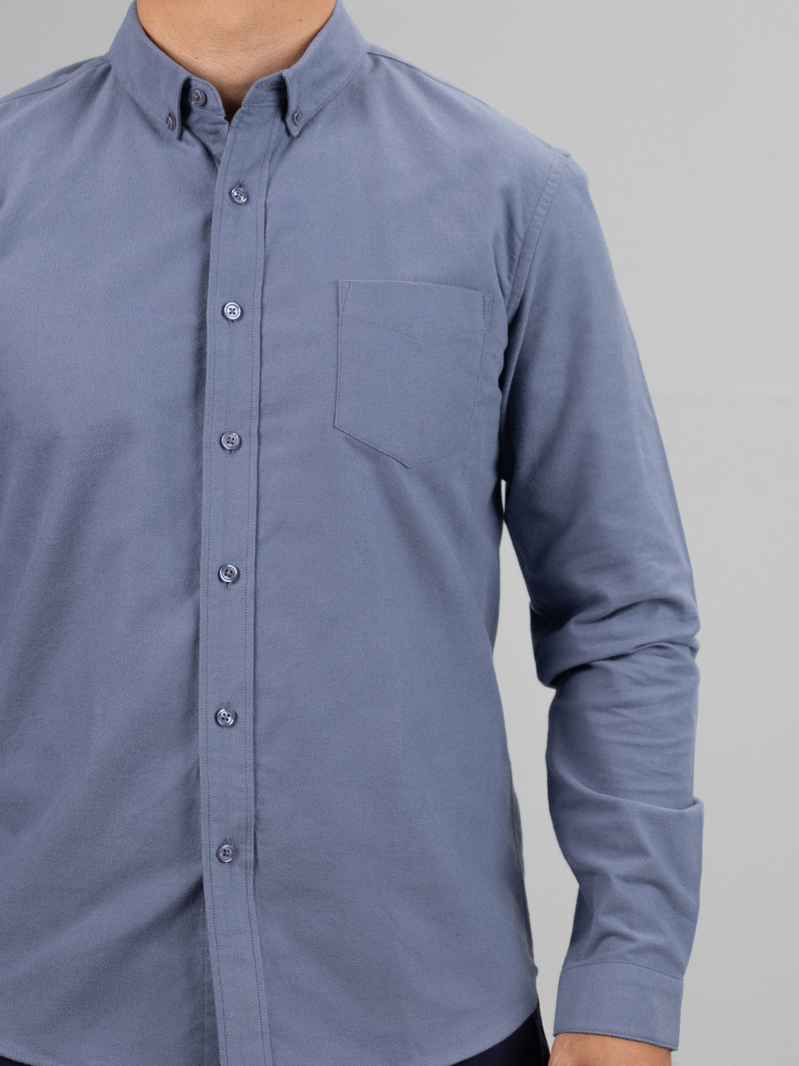 A person wearing the Milo Brushed Oxford Flannel Cotton Shirt from ID Menswear, featuring a versatile button-up design with long sleeves and a chest pocket, beautifully complements the plain gray background in a photo cropped at the shoulders, highlighting the classic style.