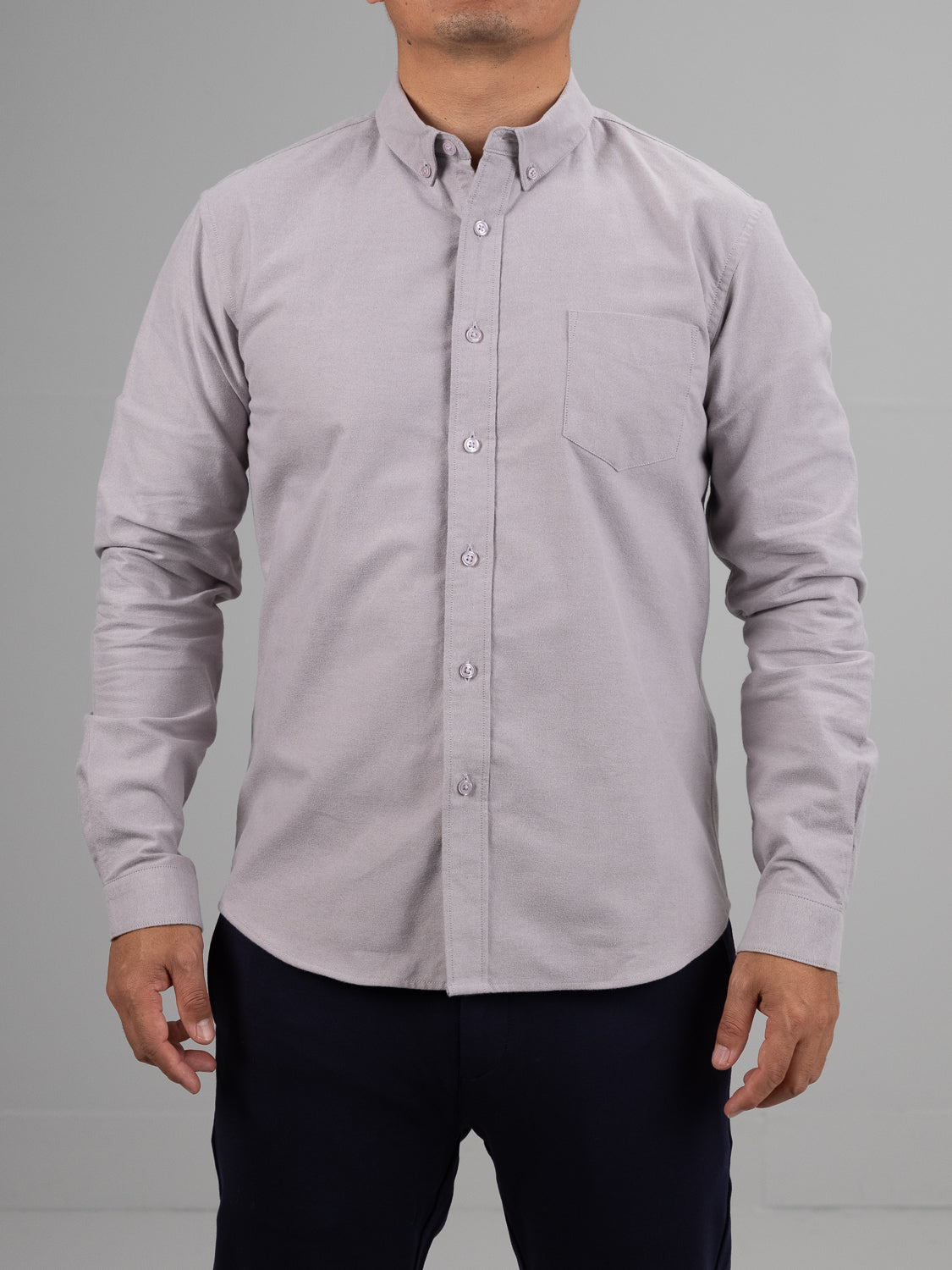 A person stands against a plain background wearing the versatile Milo Brushed Oxford Flannel Cotton Shirt in light gray by ID Menswear. This long-sleeved button-up, featuring a front pocket, is paired with dark pants for a simple yet timeless look. The head is cropped out of the image.