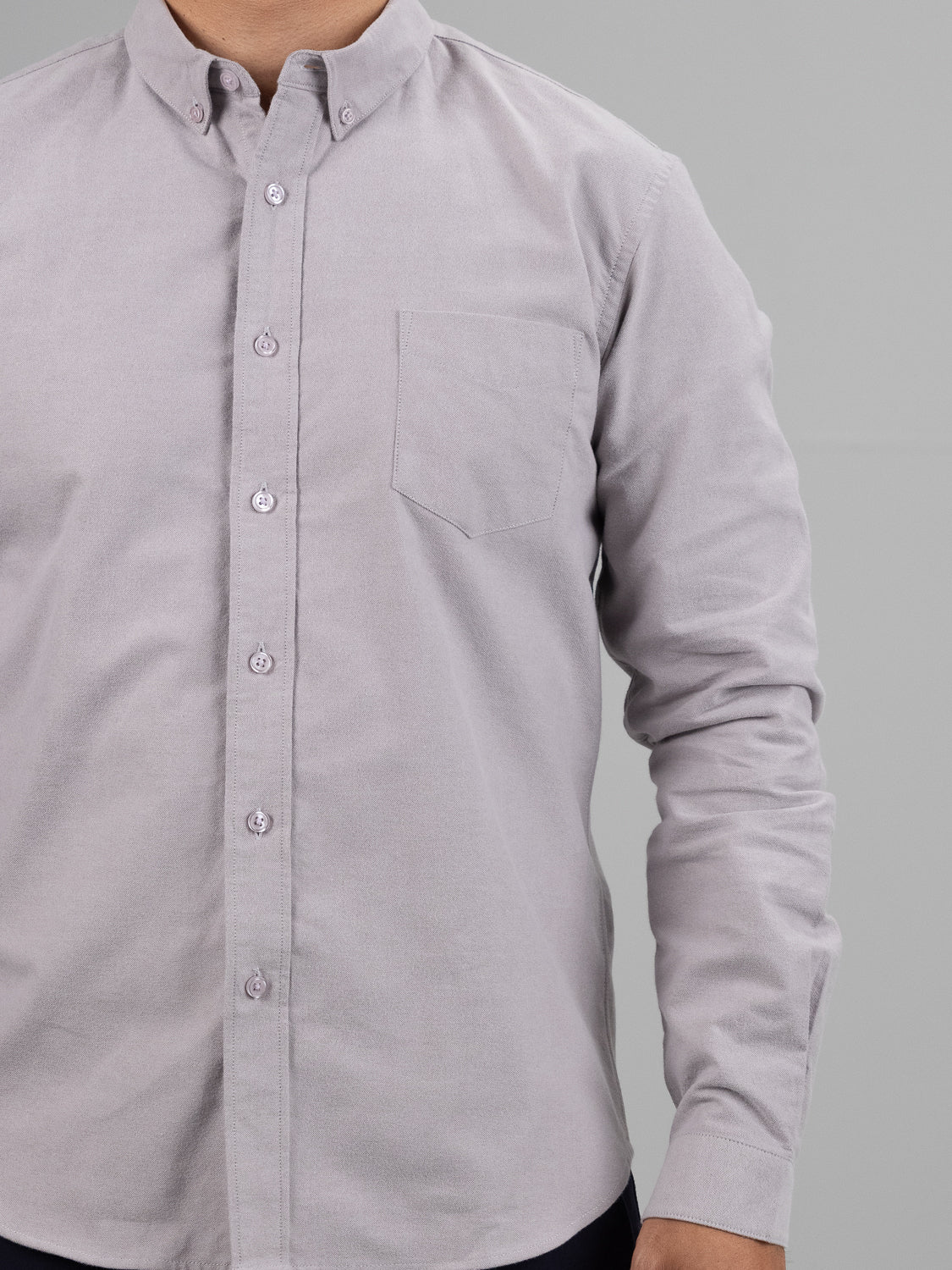 A person wears the Milo Brushed Oxford Flannel Cotton Shirt by ID Menswear, in light gray. This regular fit, crafted from 100% cotton, features a front pocket and long sleeves. The button-up design complements its classic elegance, with the image focused from shoulders to waist.
