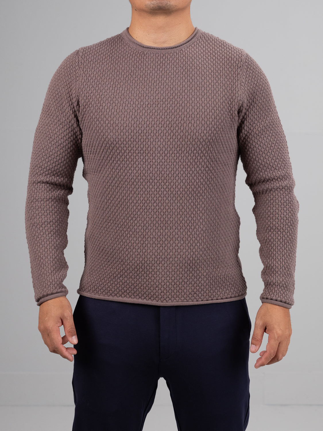 A person in an ID Menswear Westside Rolled Neck Sweater and dark pants stands against a plain gray background. The textured knitwear design keeps their arms relaxed by their sides, exuding effortless style.