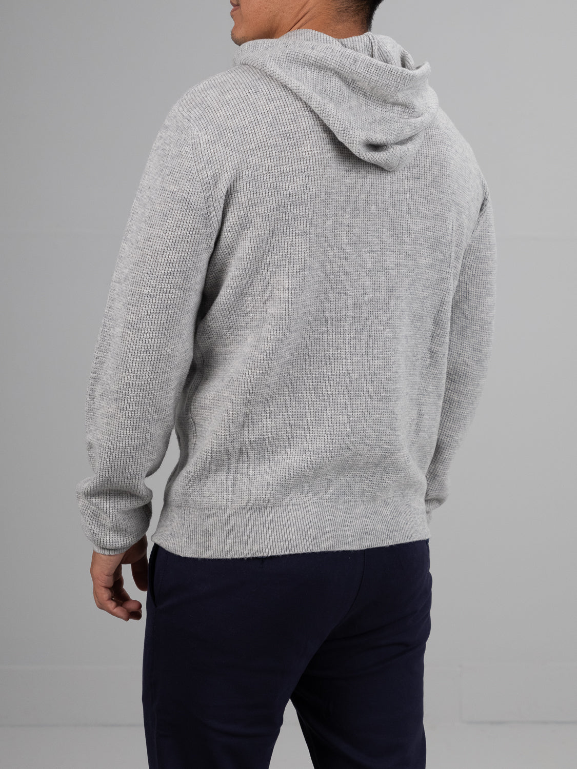 A person is shown from the back wearing the Bergen Waffle Knit Merino Hoody by ID Menswear in gray, paired with dark pants. The hoodie features a cozy, textured look similar to waffle knit, set against a plain, light-colored background.