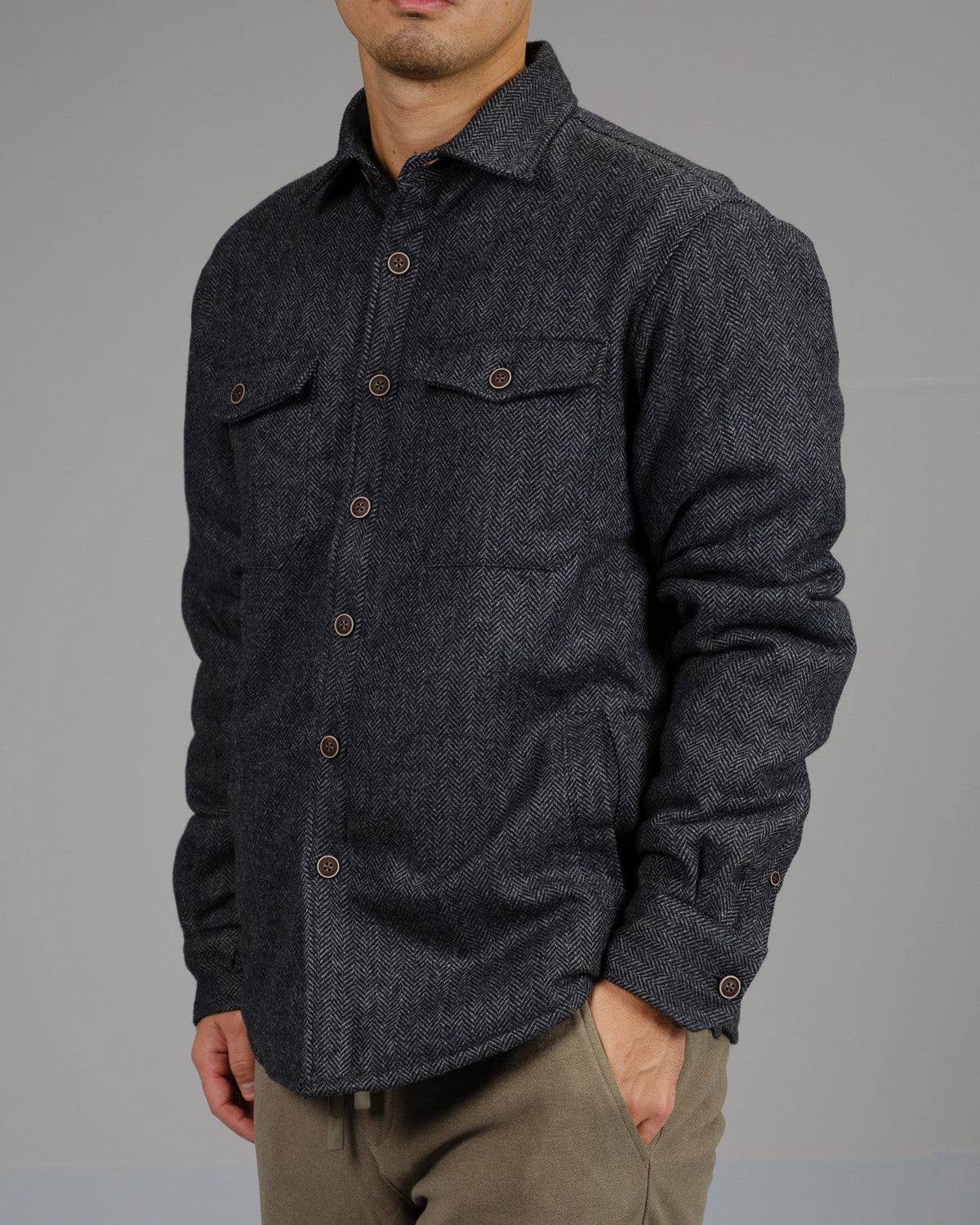 A man wears the Stuntman Wool Blend Tweed Jacket by ID Menswear—a dark gray, button-up, long-sleeve jacket with chest pockets—standing against a light gray background; perfect timeless outerwear for any occasion.