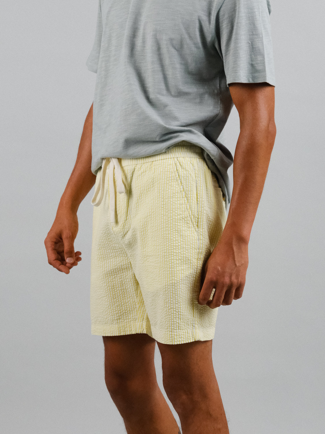A person wearing a light gray short-sleeve shirt and ID Menswears Ibiza Seersucker Drawstring Short in yellow is set against a plain gray background. Their right arm is slightly bent, highlighting an ideal warm weather outfit.