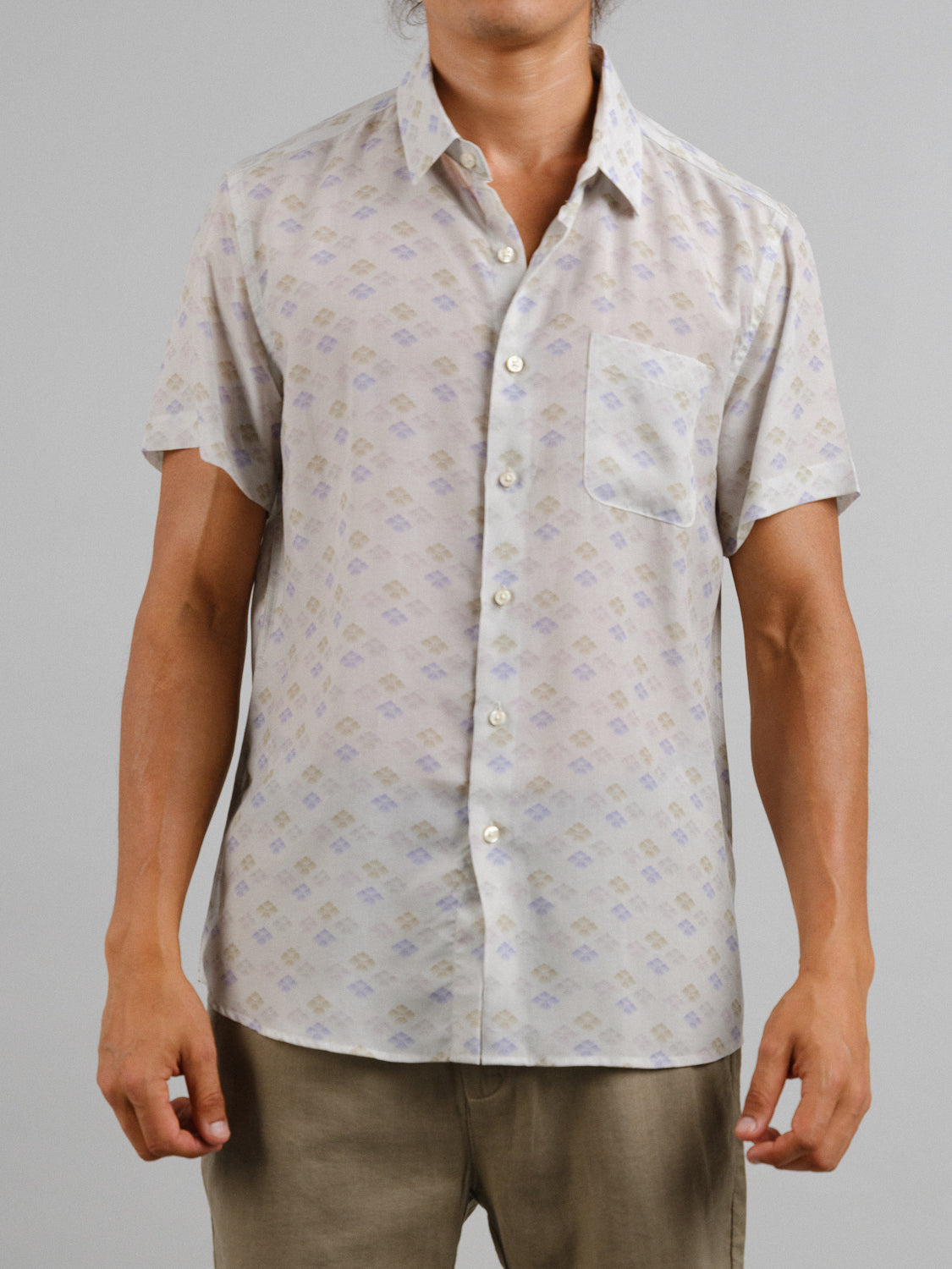 Someone wears the Hanabi Printed Tencel Linen Shirt by ID Menswear, a short-sleeve, light-colored shirt with a subtle geometric pattern and left pocket, paired with beige pants. Perfect for summer comfort against a plain gray background.