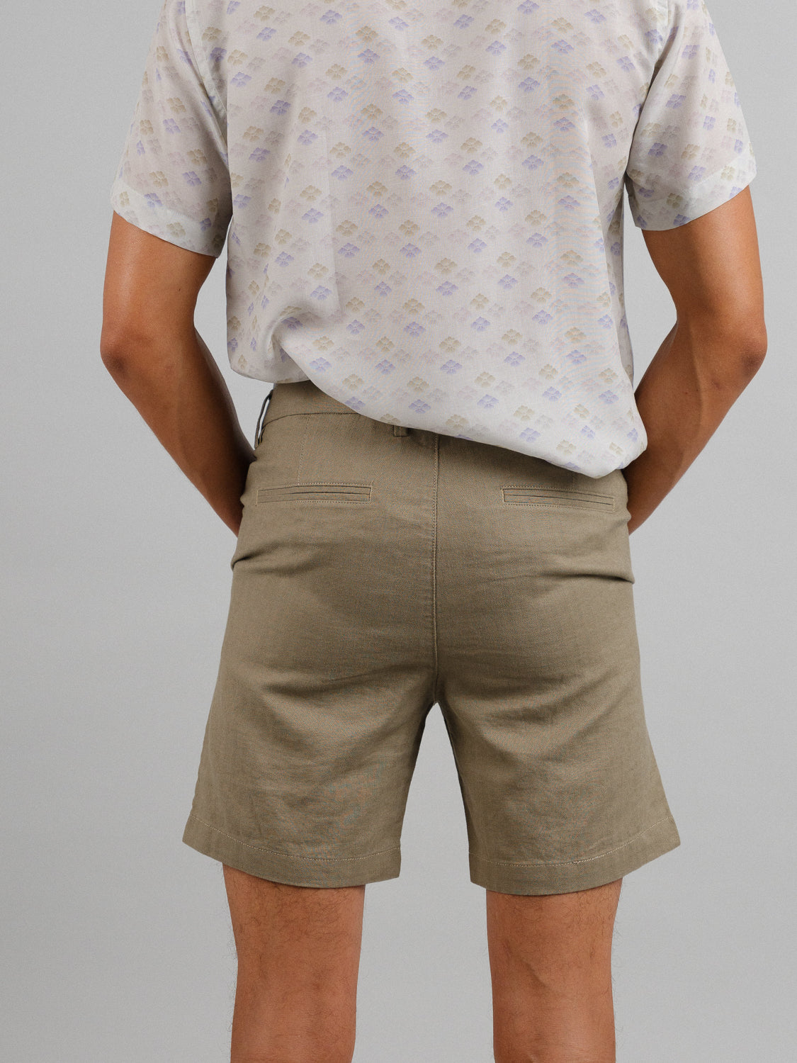 With their back to the camera, a person wears a light patterned shirt with Kerala Linen Blend Chino Shorts by ID Menswear, showcasing the relaxed fit and linen-cotton blend in khaki against a plain light gray background.