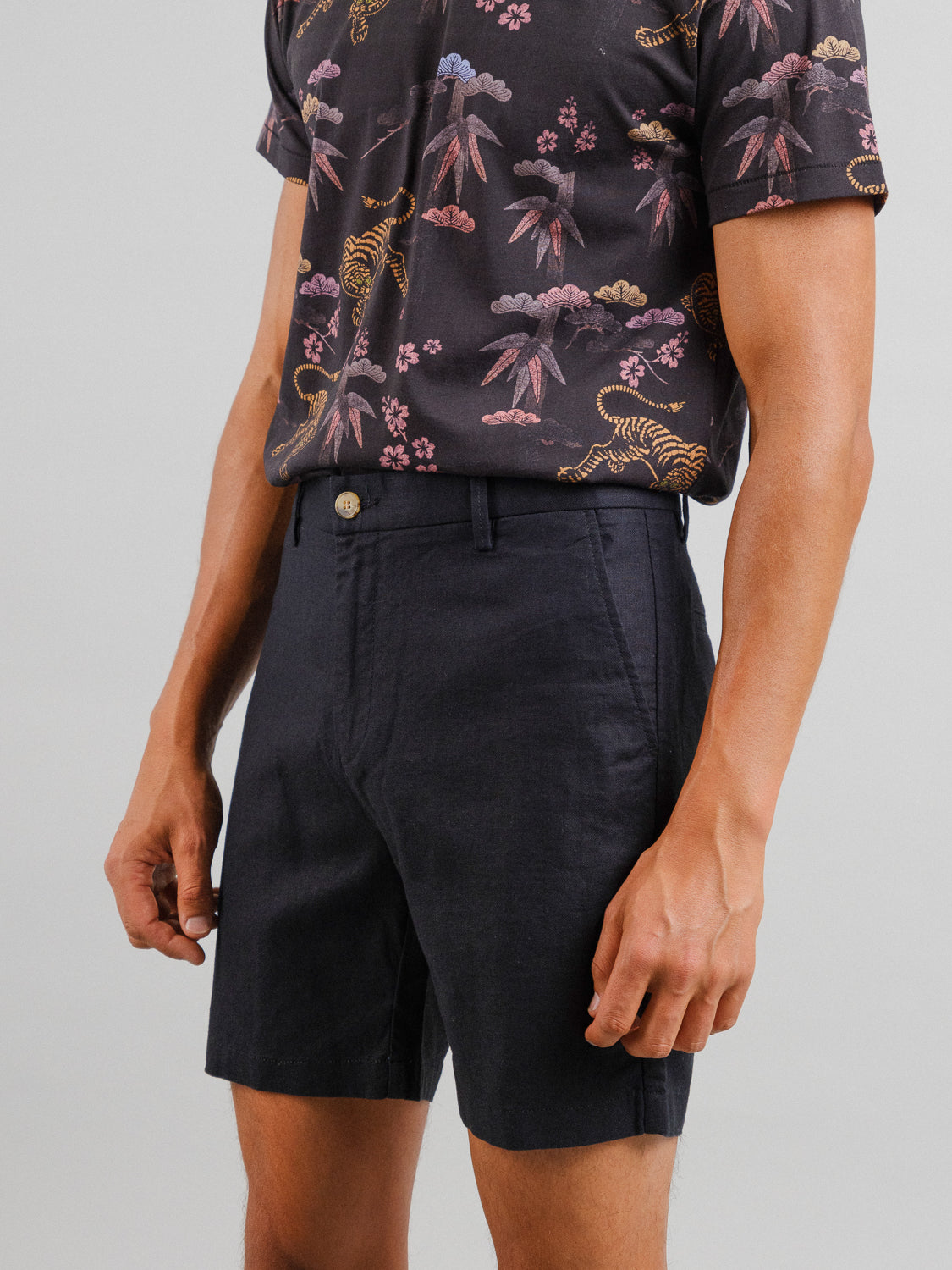 Someone is wearing the Kerala Linen Blend Chino Short by ID Menswear. The relaxed fit shorts are paired with a black shirt featuring a vibrant botanical and tiger pattern. The linen-cotton blend ensures comfort, set against a plain light gray background.