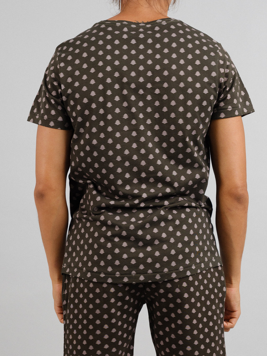 A person stands with their back to the camera, donning a matching dark outfit featuring a vintage-inspired light-colored leaf pattern. The organic cotton set from ID Menswear includes the Bali Vintage Japanese Print Tee and pants against a plain background.