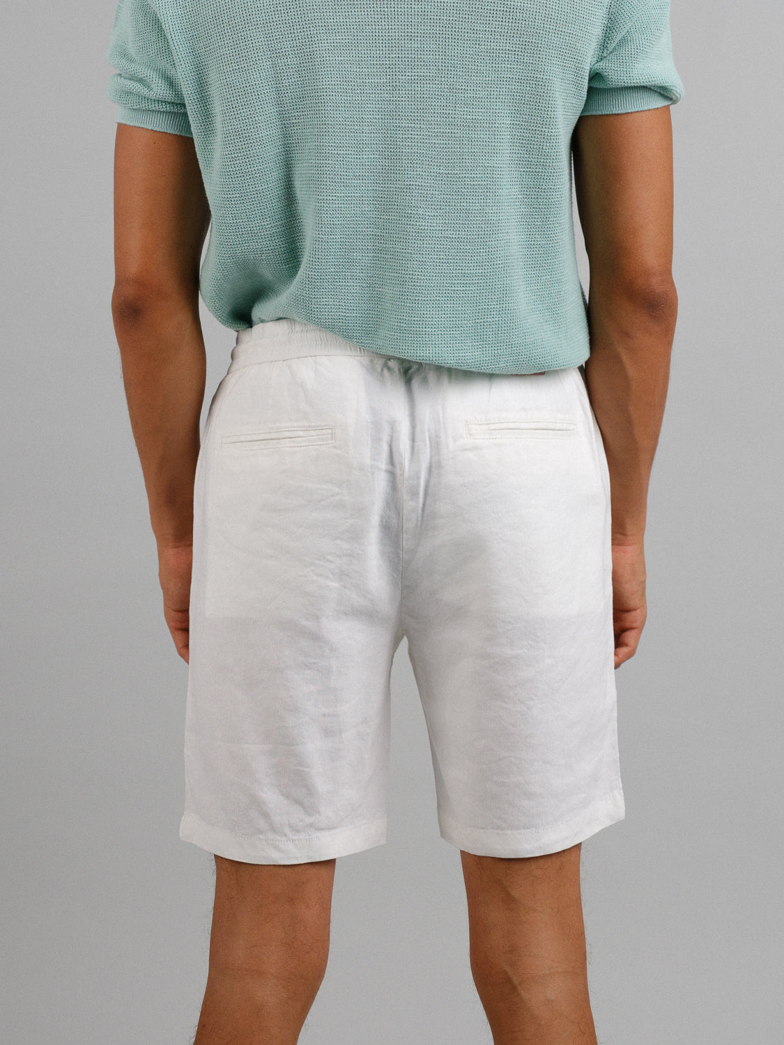 A person wearing a pastel green textured short-sleeve shirt and ID Menswears Driggs Linen Blend Short makes for a relaxing warm-weather look. The backdrop is plain gray and their hands hang casually by their sides.