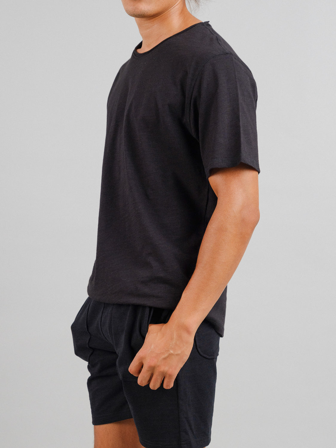 An individual in casual attire, wearing the ID Menswear Da Nang Rolled Neck Slub Tee and matching shorts, stands against a plain gray background. They are facing slightly left, with their right arm visible.