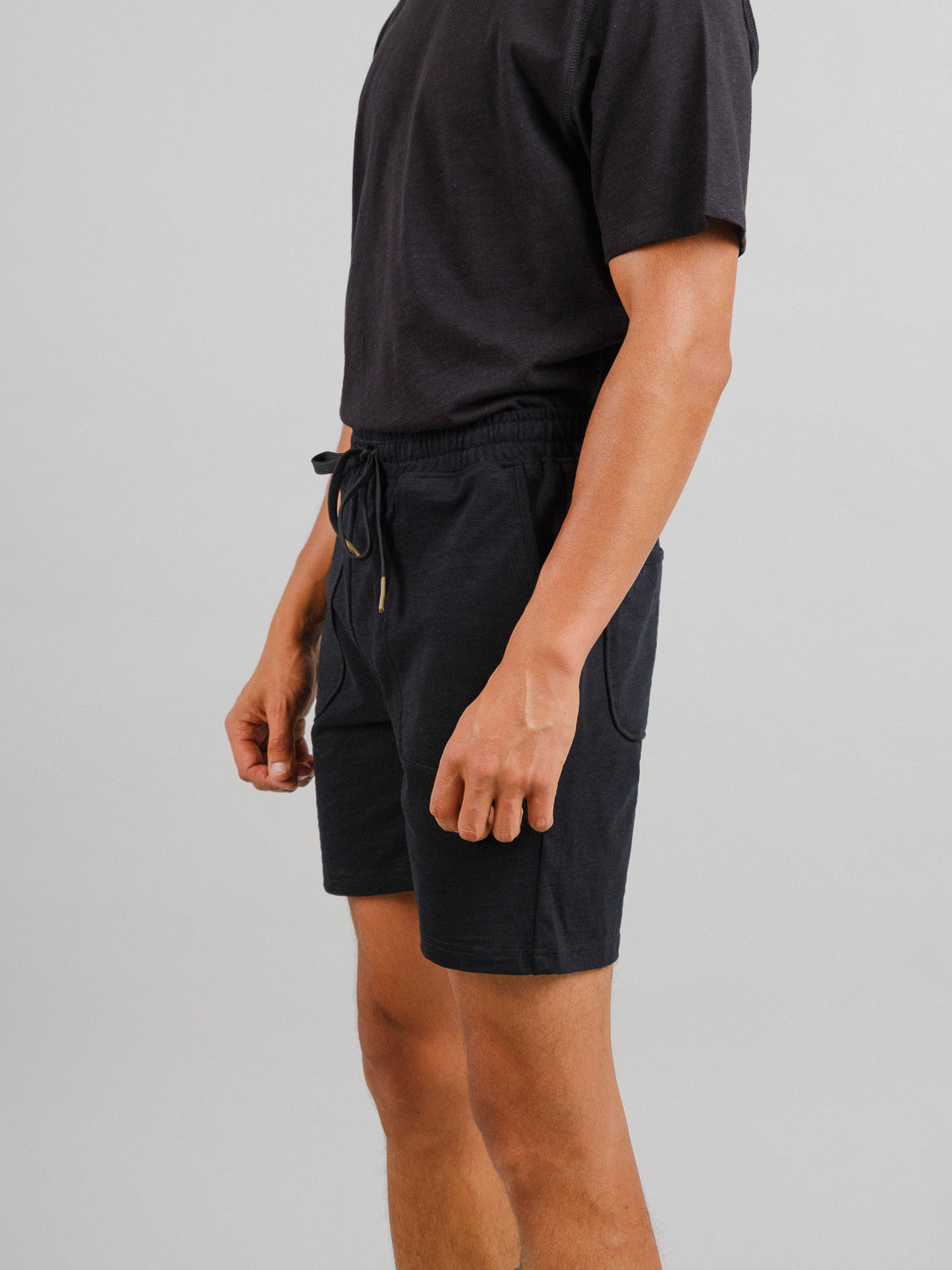A person in a black slub cotton T-shirt and ID Menswears Kahala Slub Cotton Drawstring Shorts is posed against a plain background, showcasing the outfit from neck to knees with an emphasis on the side profile.