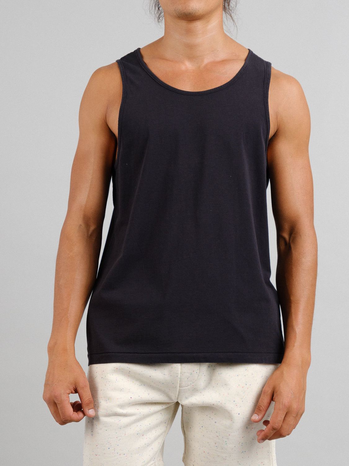 A person wears an ID Menswear Settler Snow Vintage Wash Tank Top with light-colored pants against a neutral backdrop, exuding a subtle vintage vibe. The image does not show their head.