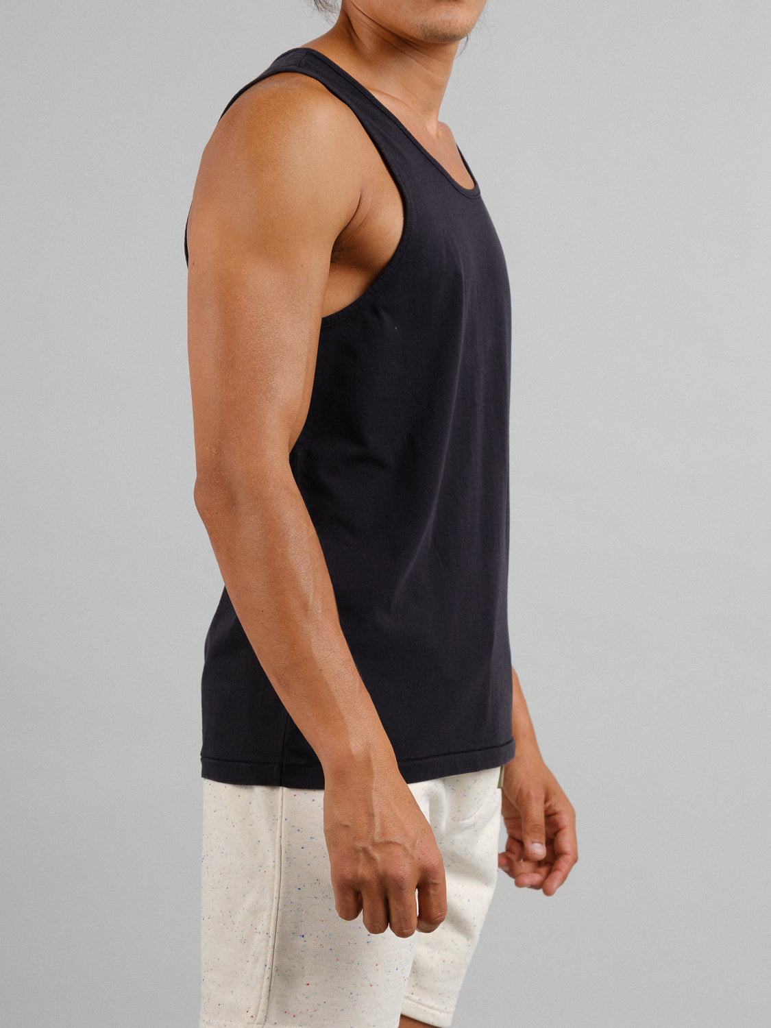 A person wearing an ID Menswear Settler Snow Vintage Wash Tank Top and light-colored shorts stands in a vintage look against a plain gray background, showcasing their left side while facing slightly to the right.