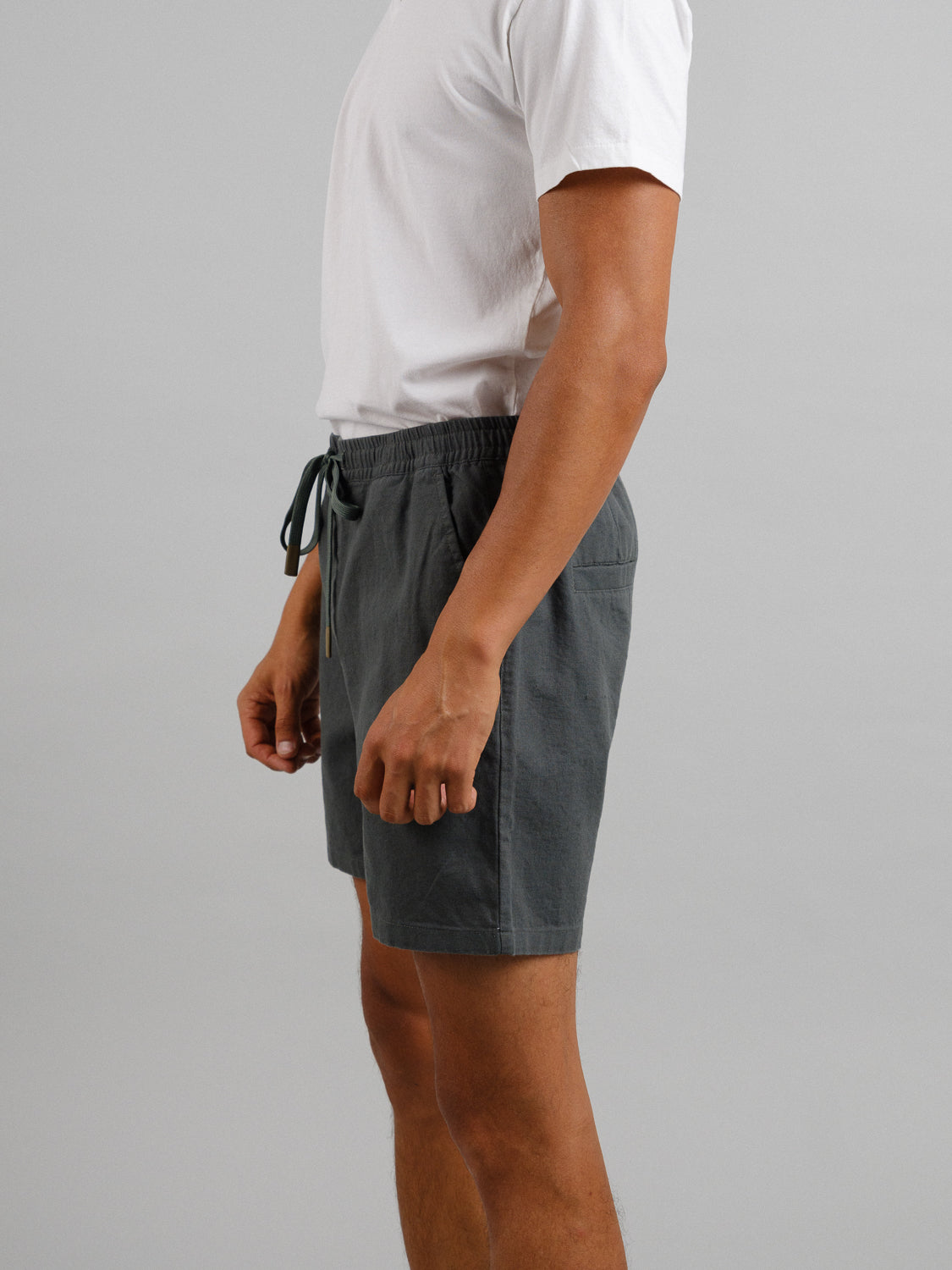 A person in a white t-shirt and Kotao Linen Blend Drawstring Short by ID Menswear stands against a neutral background. The gray summer shorts feature an elastic waistband with a drawstring. The persons upper body is cropped out of the image.