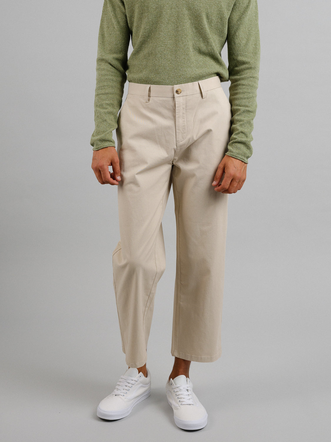 A person is wearing a light green long-sleeve shirt, ID Menswears Bigboy Relaxed Flooded Chino in a casual cut, and white sneakers. They stand against a plain gray background with one leg slightly forward, maintaining a lightweight look.