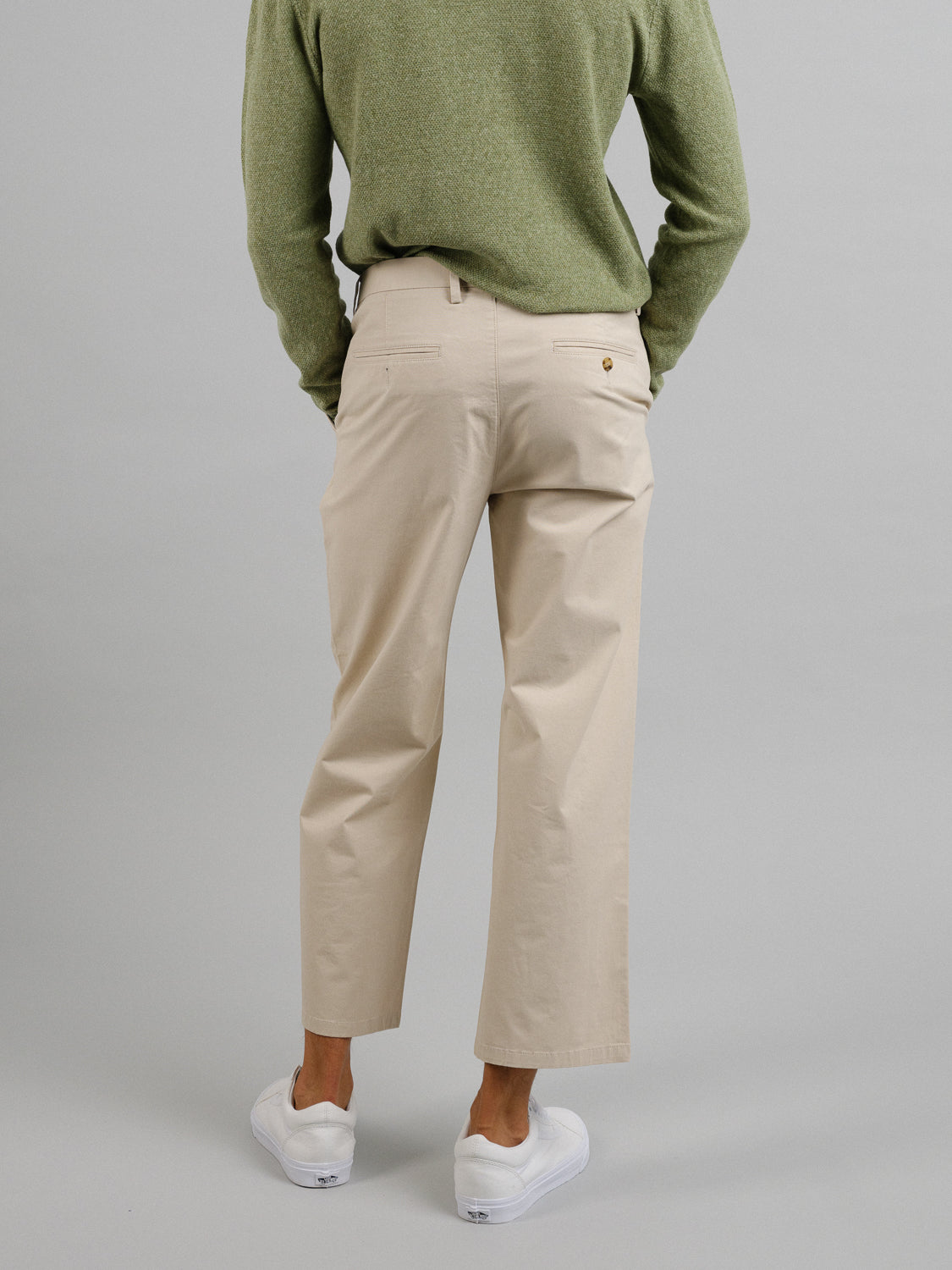 A person stands against a plain gray background wearing a green sweater, white sneakers, and the Bigboy Relaxed Flooded Chino pants from ID Menswear.