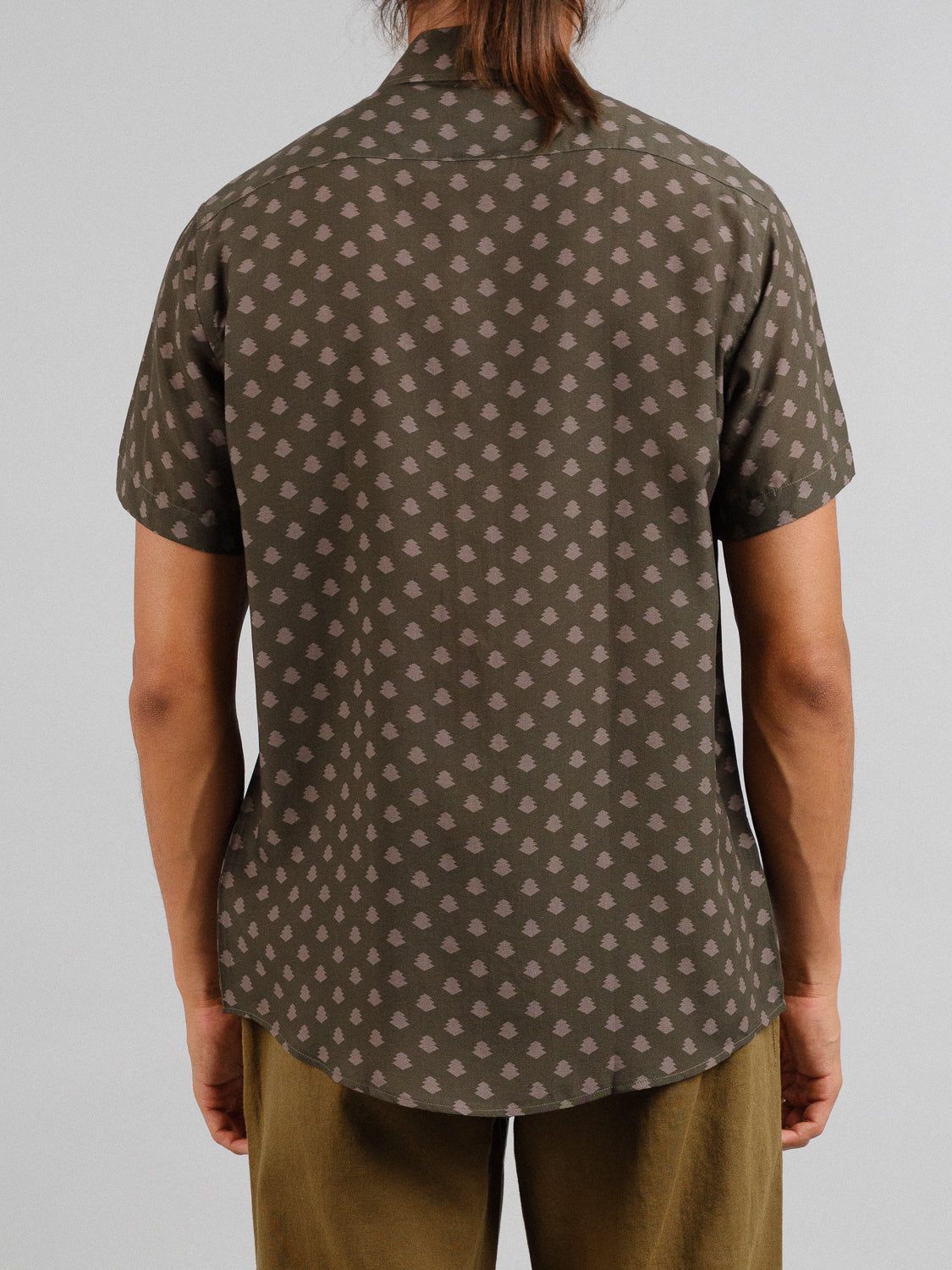 A person viewed from the back against a plain backdrop showcases ID Menswears Ogawara Printed Tencel Linen Shirt in dark green with a cloud-like pattern, paired with tan pants, as the ultimate summer wardrobe staple.