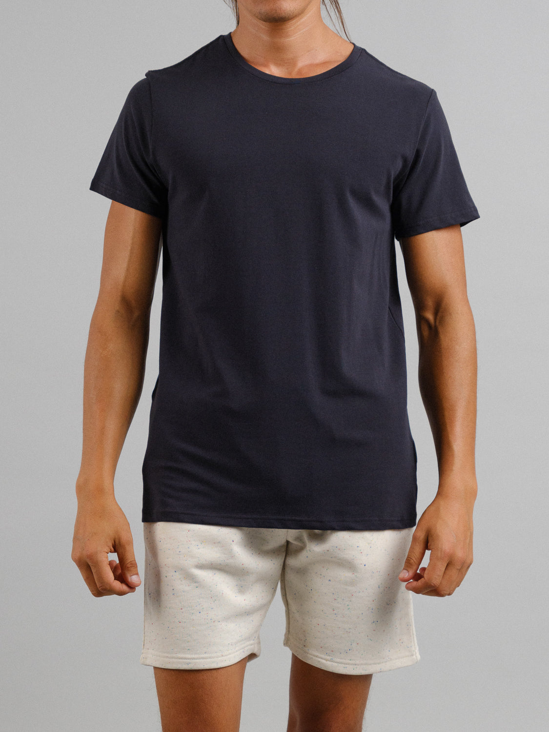 A person models the Form Crew Neck Tee in black from ID Menswear, paired with beige shorts. They stand against a neutral background, arms relaxed, highlighting the tees comfortable fabric and casual style.