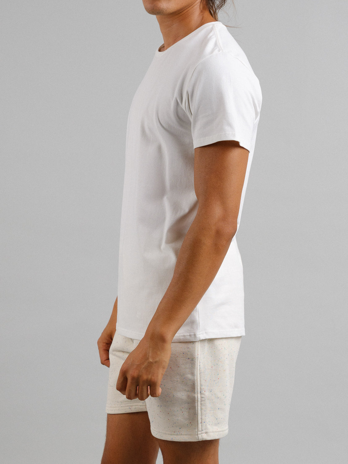 An individual wearing the ID Menswear Form Crew Neck Tee and light-colored shorts stands sideways against a neutral gray backdrop.