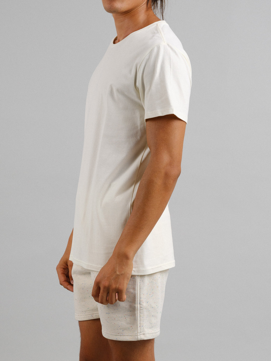 A person wearing a plain light-colored, form-fitting ID Menswear Form Crew Neck Tee and matching shorts stands against a neutral background, shown from the side. The ensemble, made from comfortable fabric, exudes effortless style.