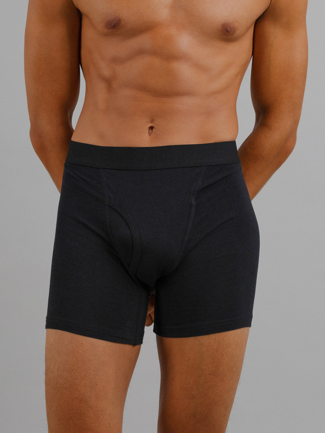 A person models black ID Organic Cotton Boxer Briefs from ID Menswear against a gray background, highlighting their fit and style. These everyday essentials showcase stretch, design, and structure.