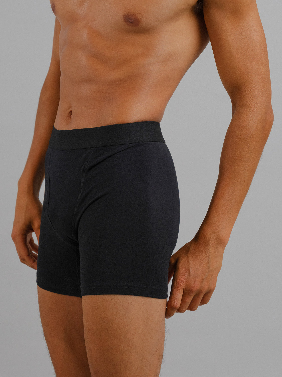 A person is shown from the waist down wearing ID Menswears black organic cotton boxer briefs against a neutral gray background. Their right arm rests at their side, showcasing the ID Organic Cotton Boxer Briefs 3 Packs stretch and comfort.
