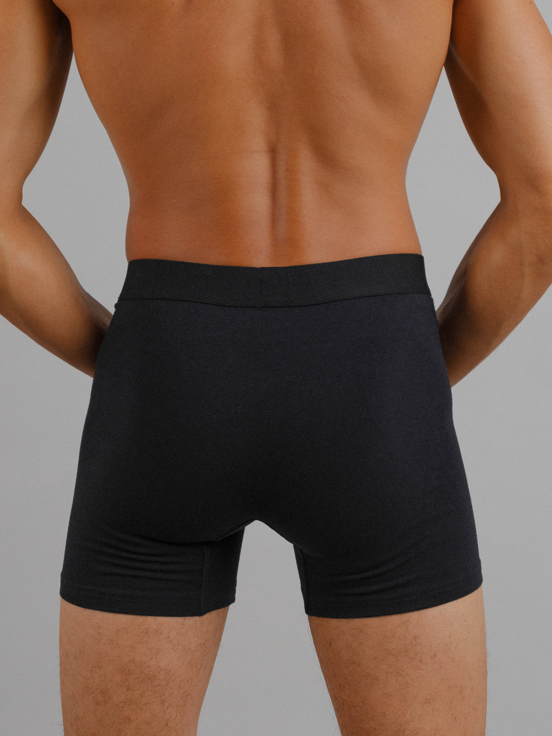 A person with a muscular build is shown from the back wearing ID Menswears black Organic Cotton Boxer Briefs, everyday essentials offering comfort and style. The plain gray background emphasizes their perfect stretch fit.