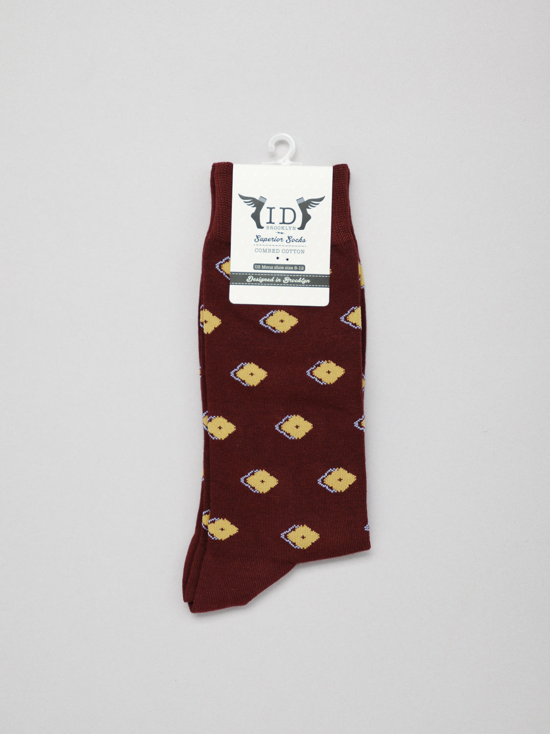 A maroon Keda Graphic Sock from ID Menswear, featuring small yellow bear faces, is shown on a white background. Made of combed cotton for comfort, it has a label near the top with text and a winged logo.