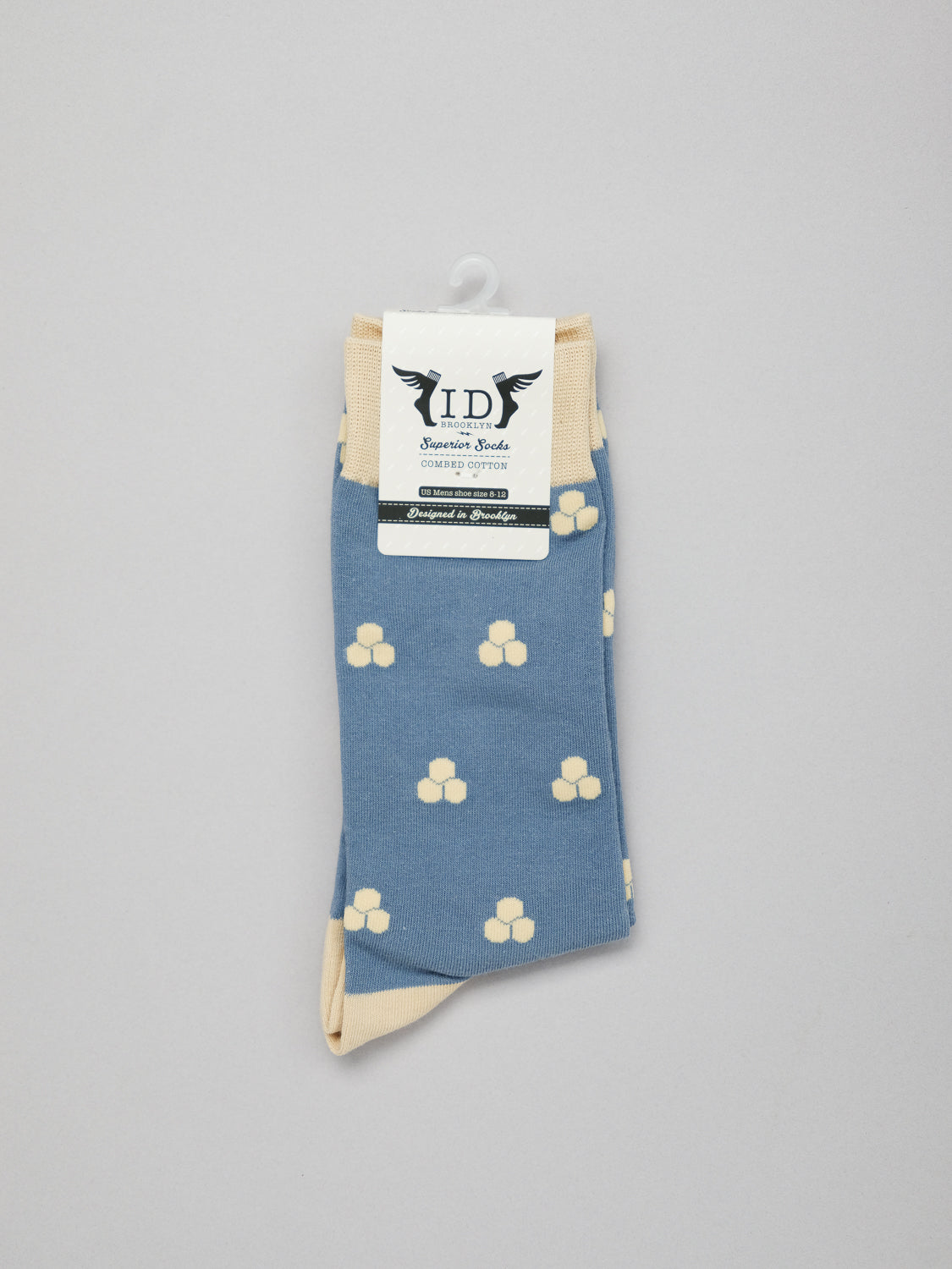 Mae Graphic Socks by ID Menswear are blue with a Japanese pattern of cream flowers, made from premium combed cotton for comfort. Featuring cream cuffs and toes, theyre neatly folded and attached to a white hanger with a label on top, set against a light gray background.